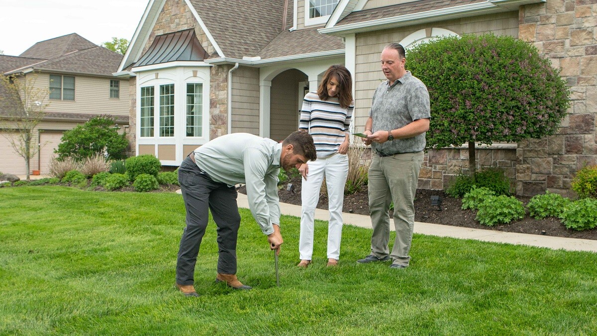 technician on lawn with customers looking at grass testing soil 