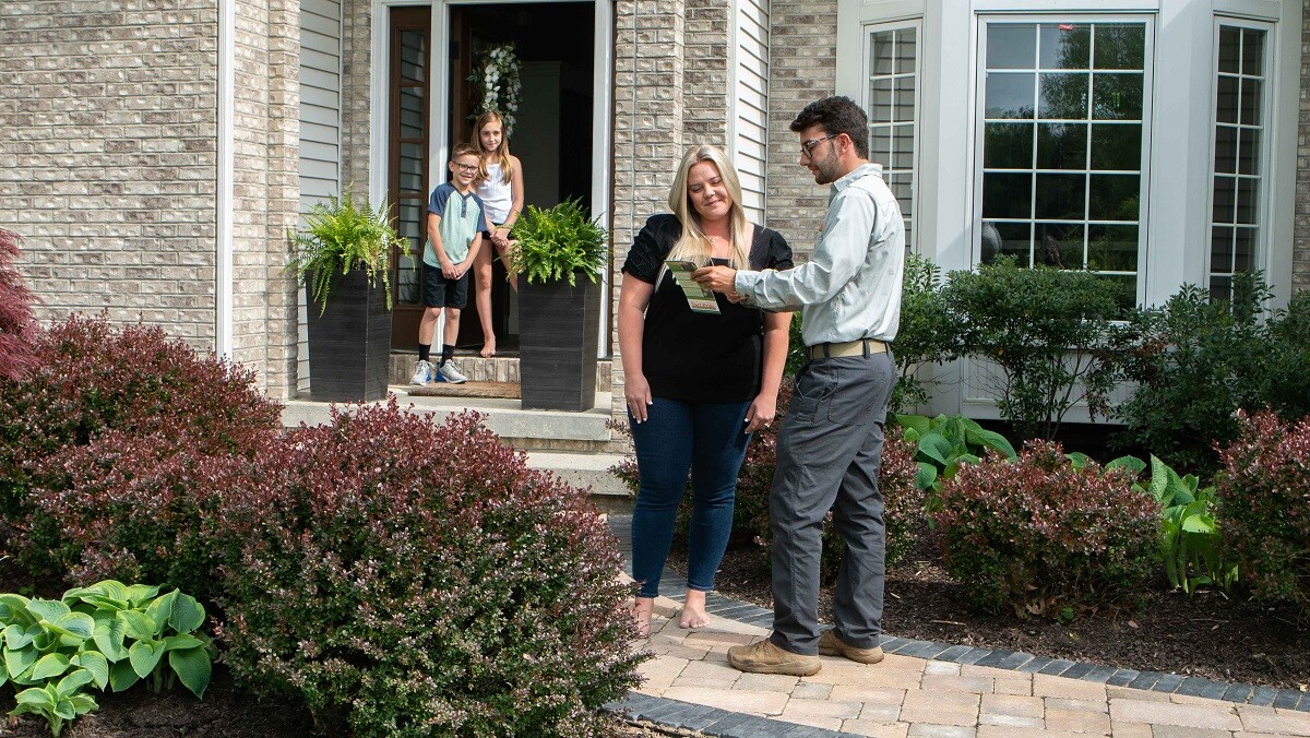 technician showing customer yard treatment options with kids in background